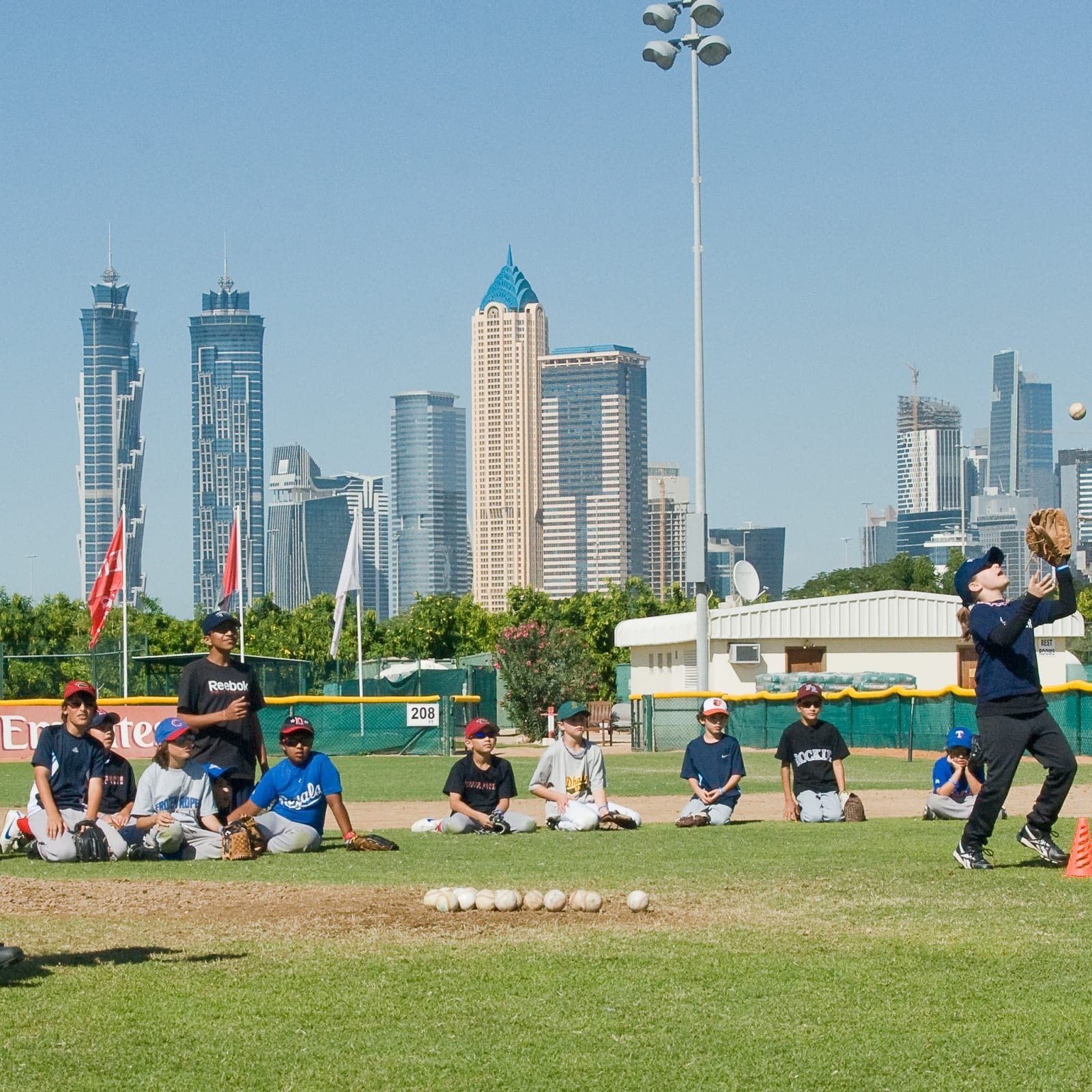 A Frozen Ropes camp on an international field, kids fielding with a city skyline behind them